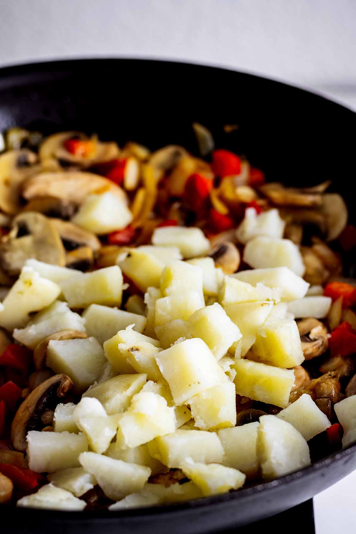 Potatoes cooking in a skillet with onions, mushrooms and red pepper.