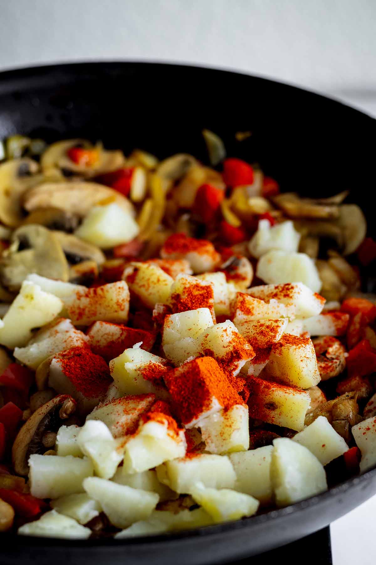 Paprika added to pan with potatoes, onions, mushrooms and red pepper.