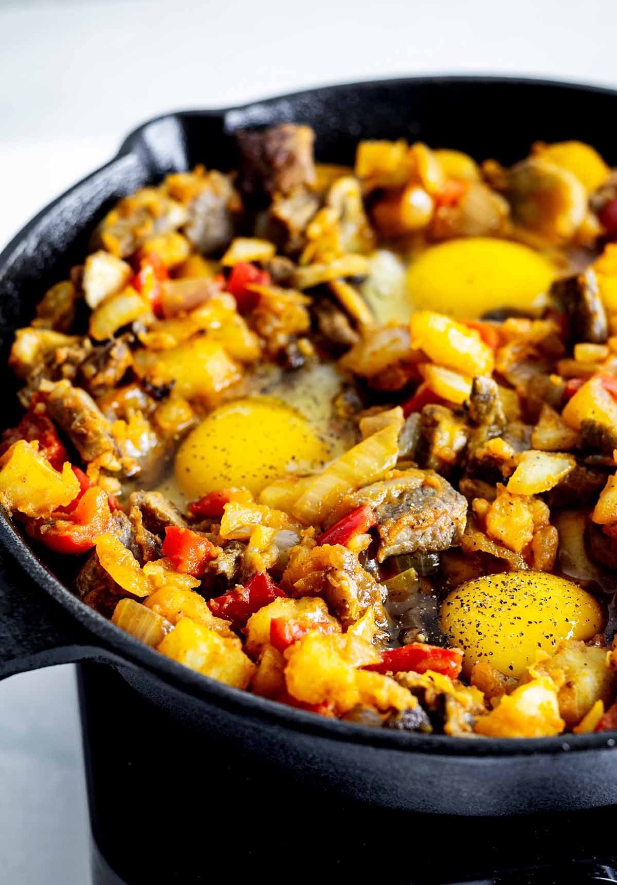 Raw eggs in skillet with steak and vegetables.