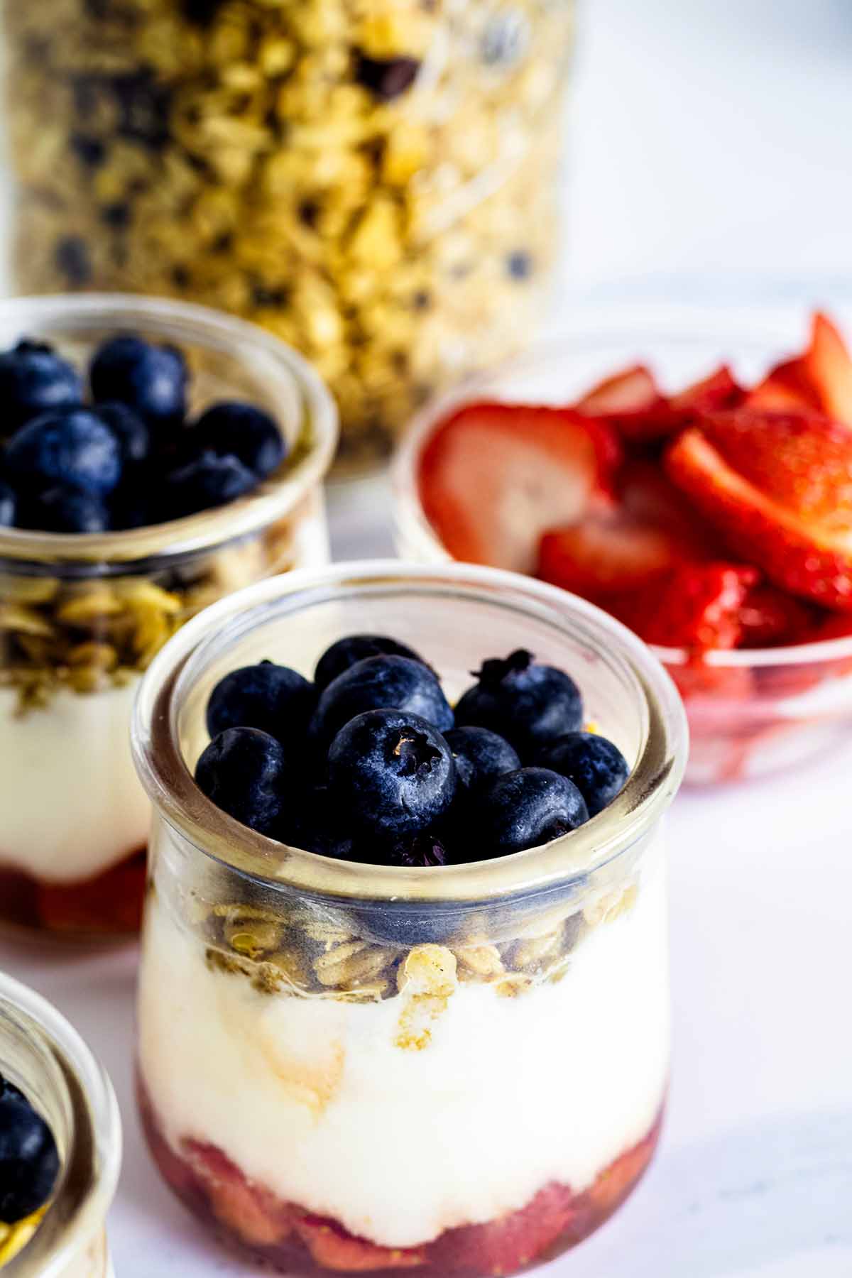 Two parfaits in glass jars with sliced strawberries and a jar of granola