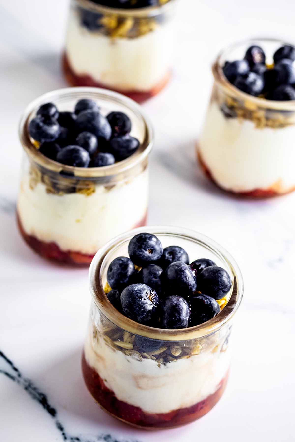Blueberries on top of four yogurt parfaits in glass jars