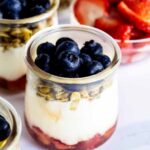 Close up of berry yogurt parfait in a glass jar with sliced strawberries