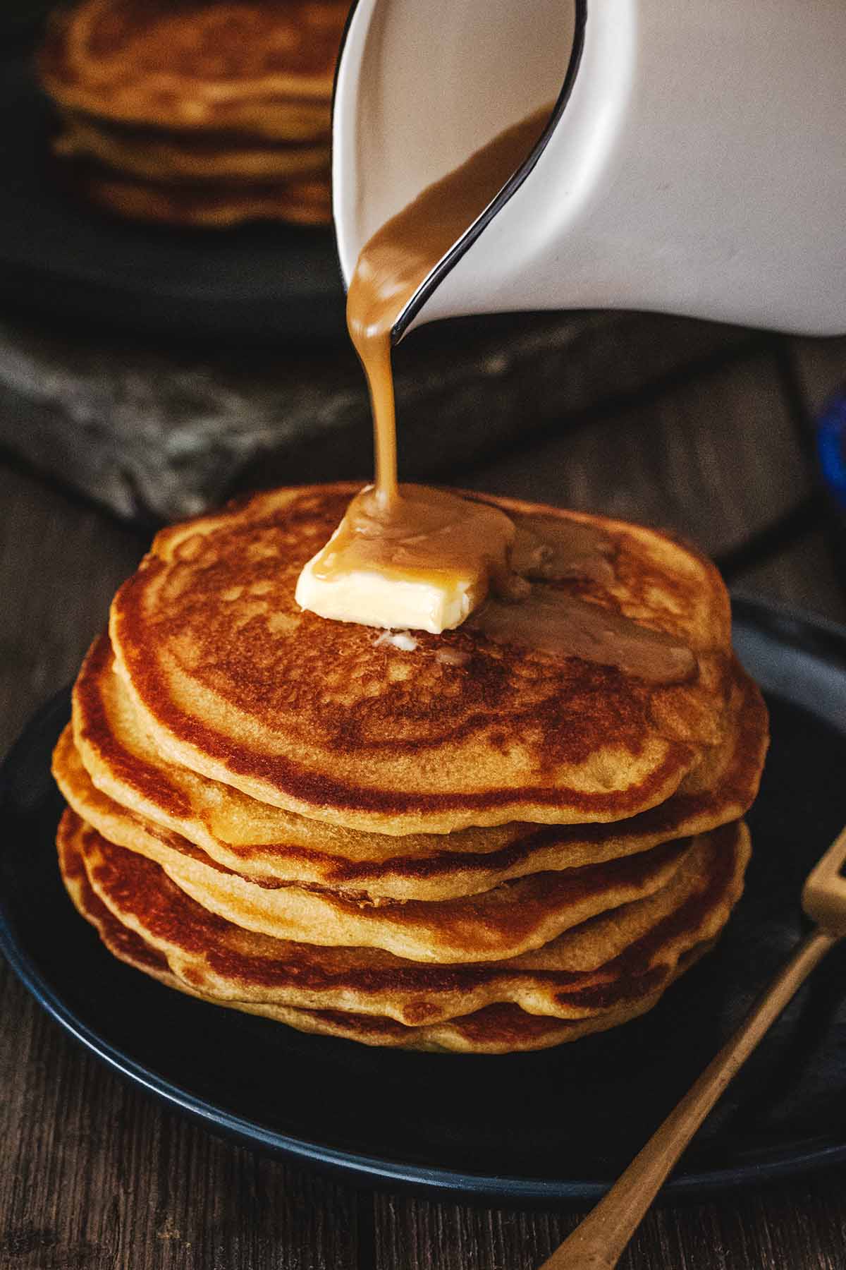 Butterscotch sauce being poured on a stack of butterscotch pancakes