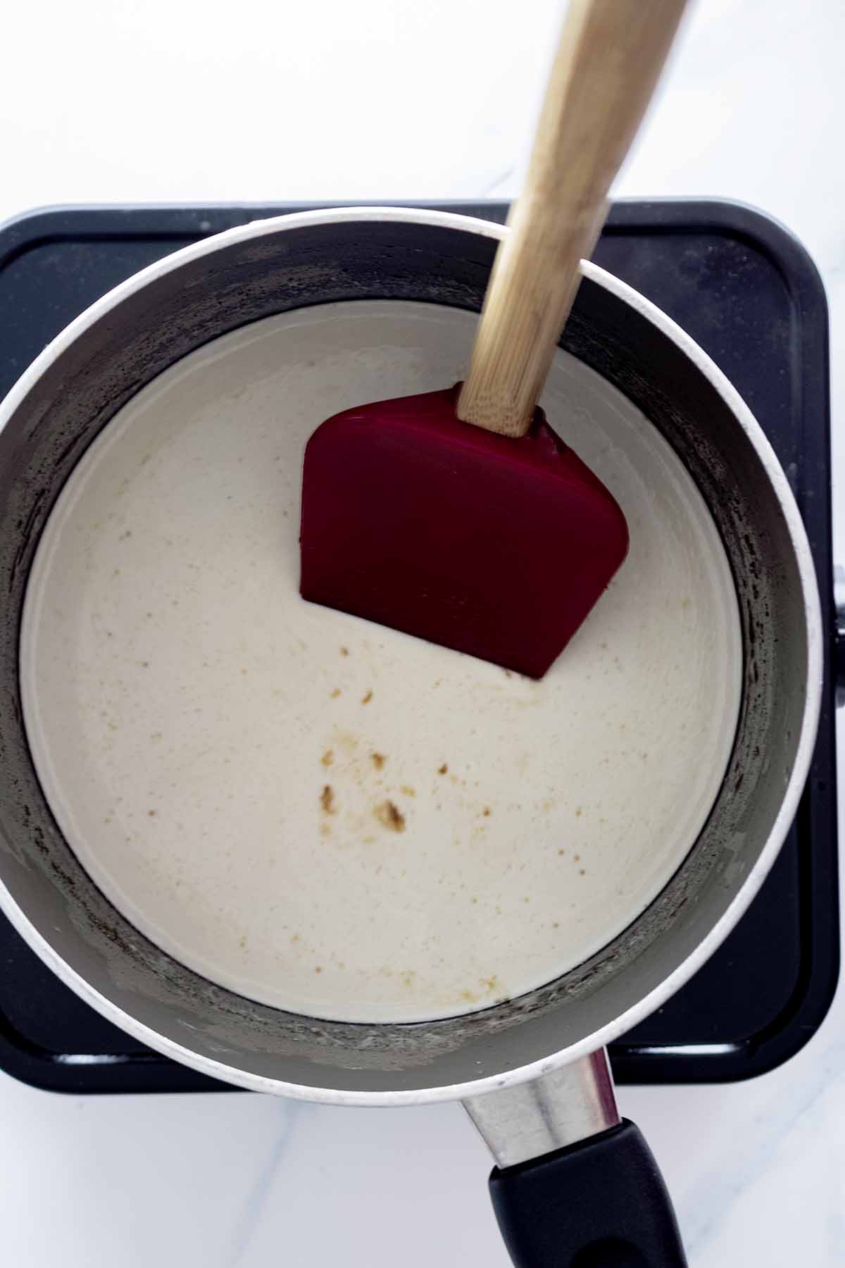 Heavy cream in a saucepan with a red spatula.