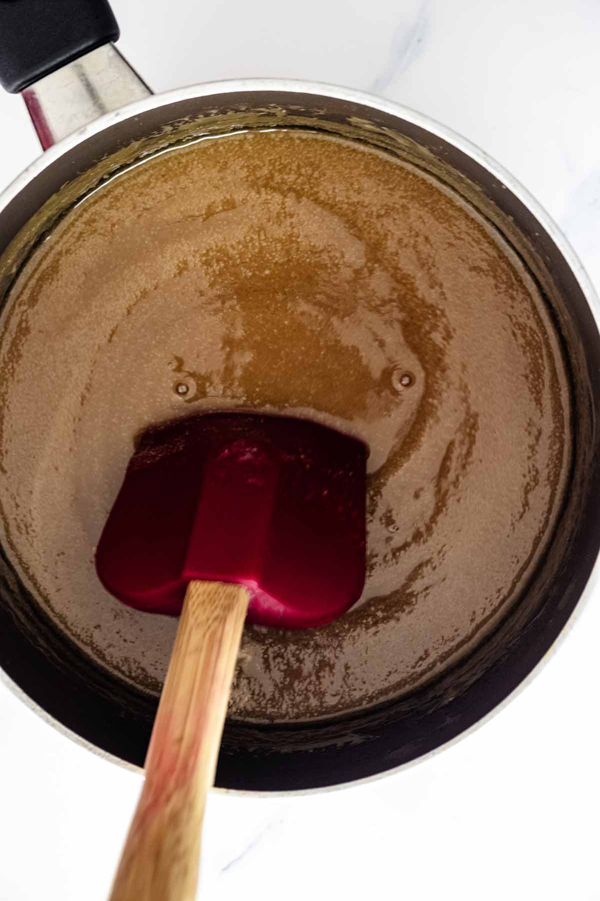 Red spatula stirring butterscotch mixture in a saucepan
