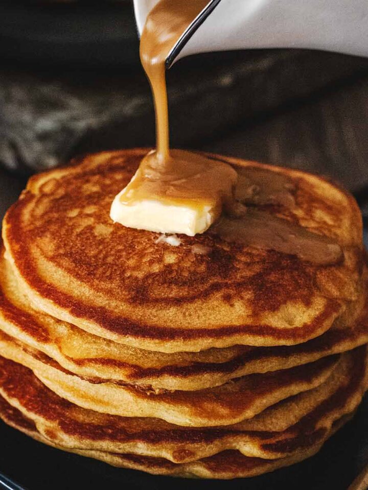 Butterscotch sauced being poured over a stack of butterscotch pancakes
