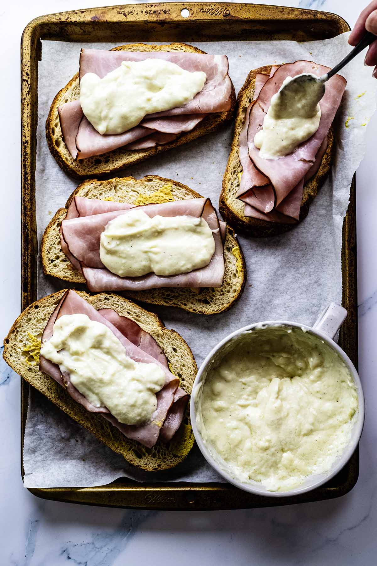 Spreading croque madame sauce on top of ham on four sandwiches