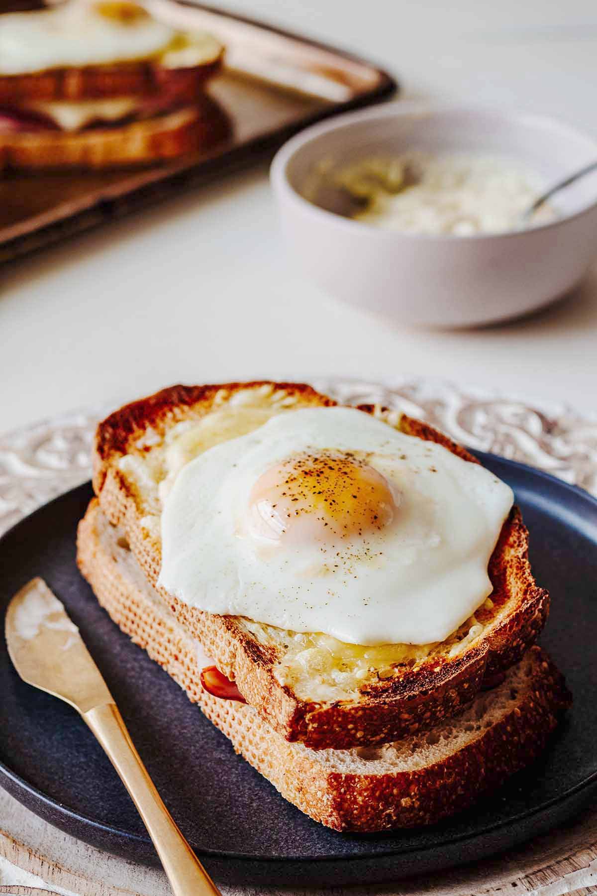 Croque madame on a grey plate with a gold knife.