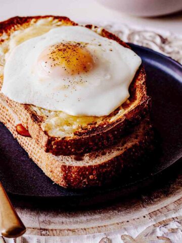 Croque madame on a grey plate with a gold knife.