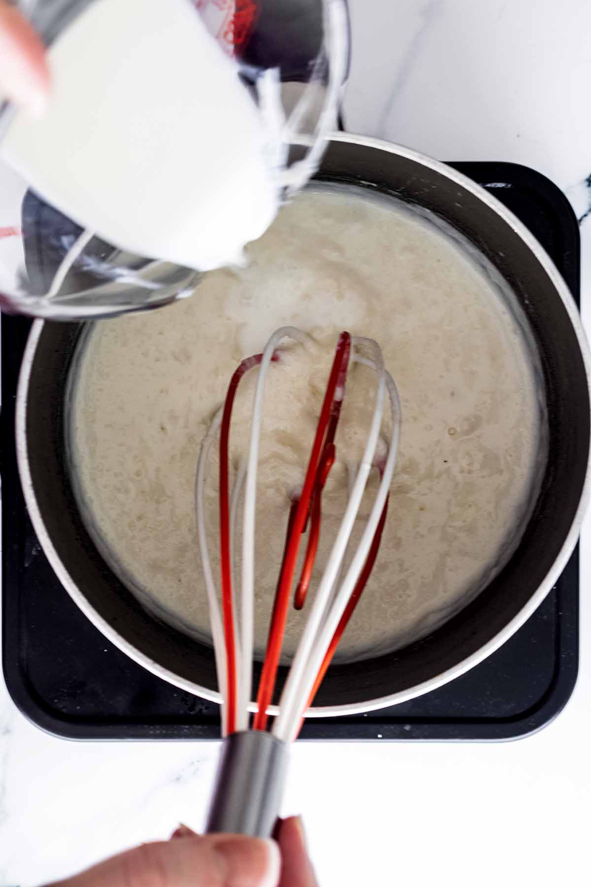 Milk being whisked into a saucepan