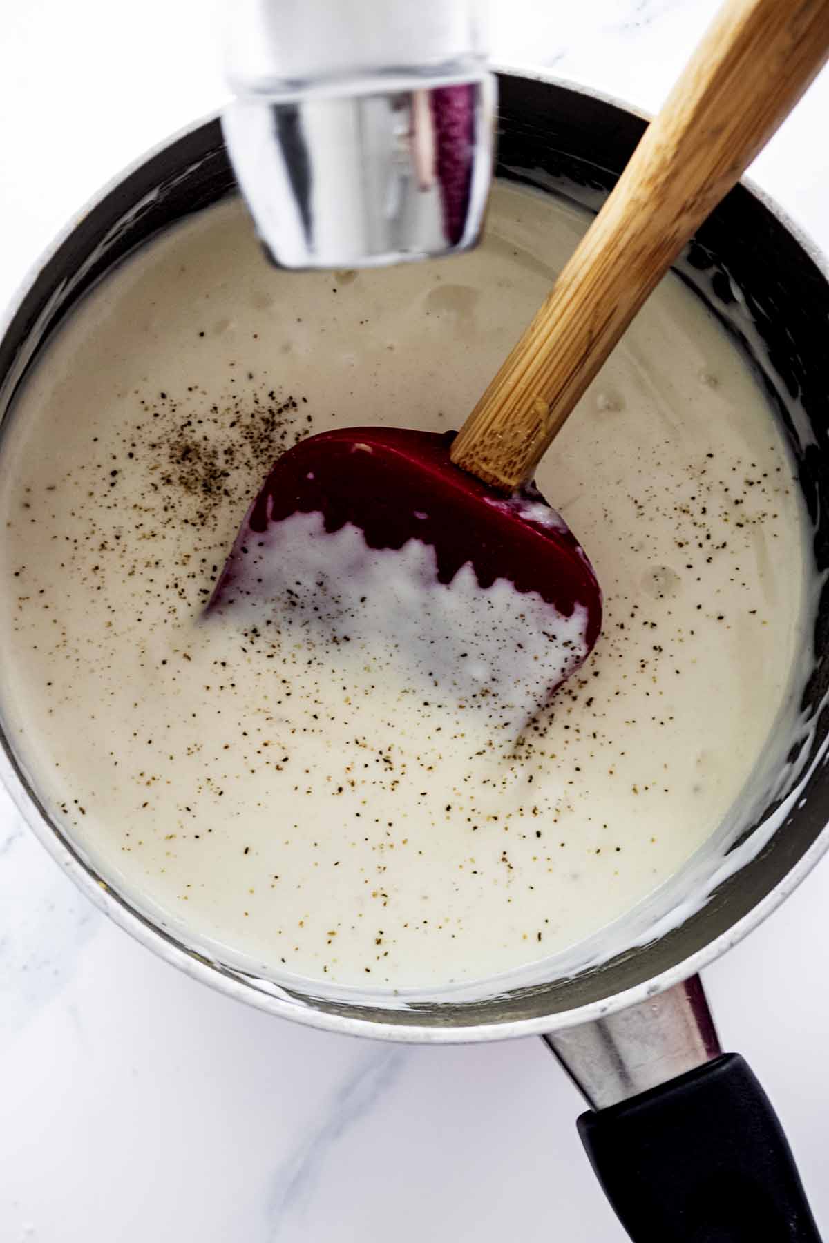 Salt being added to sauce in a saucepan with a spatula
