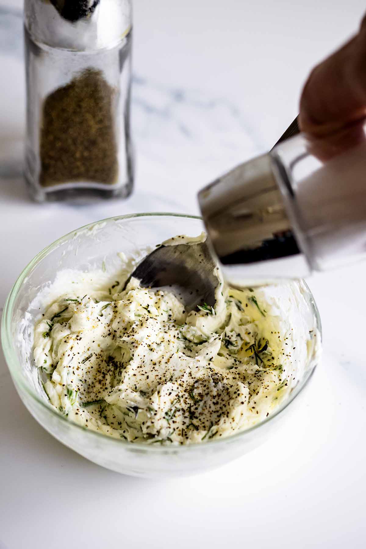 Adding salt to a bowl of herbed cream cheese