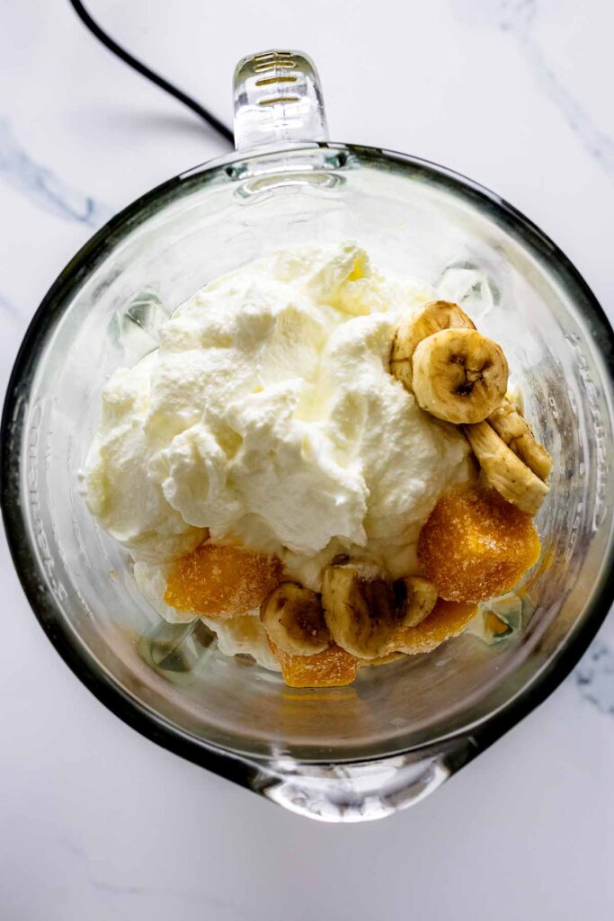 Overhead view of yogurt, bananas and frozen mango in a blender.