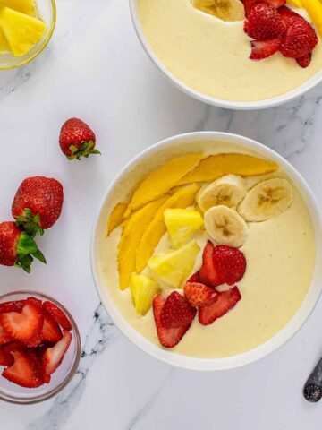 Overhead view of smoothie bowls with strawberries and pineapple.