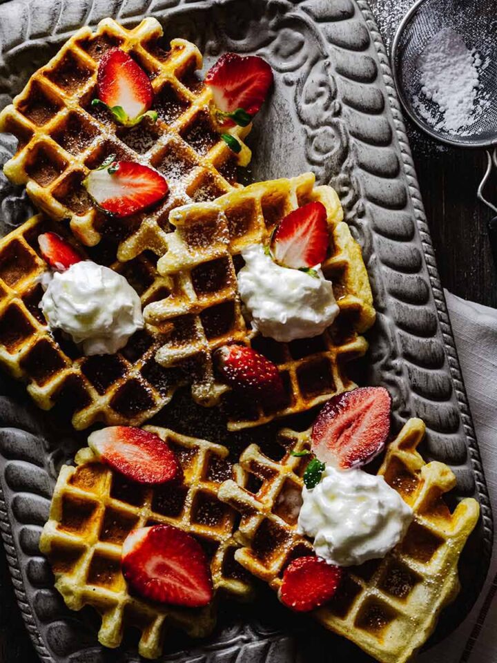 Overhead view of buttermilk Belgian waffles on a gray tray with strawberries and whipped cream