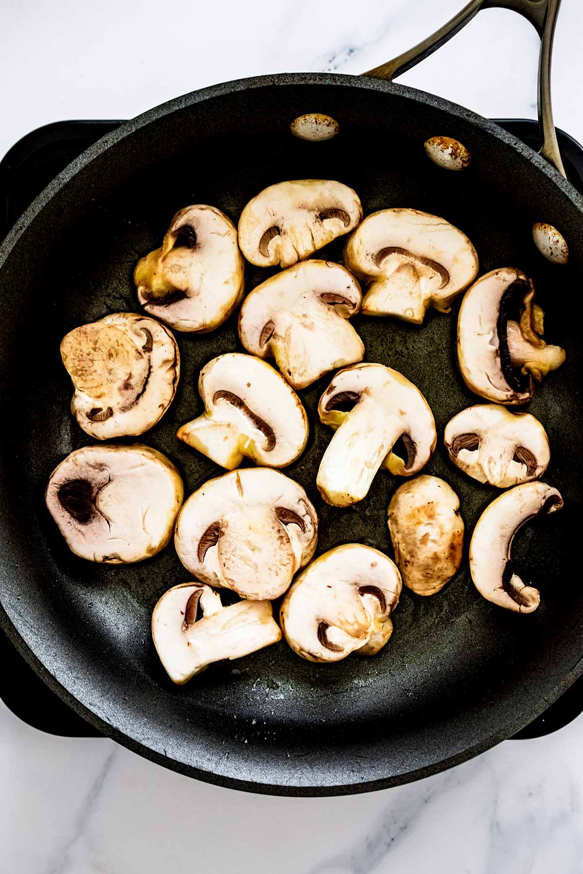 Overhead view of sliced mushrooms cooking in a skillet
