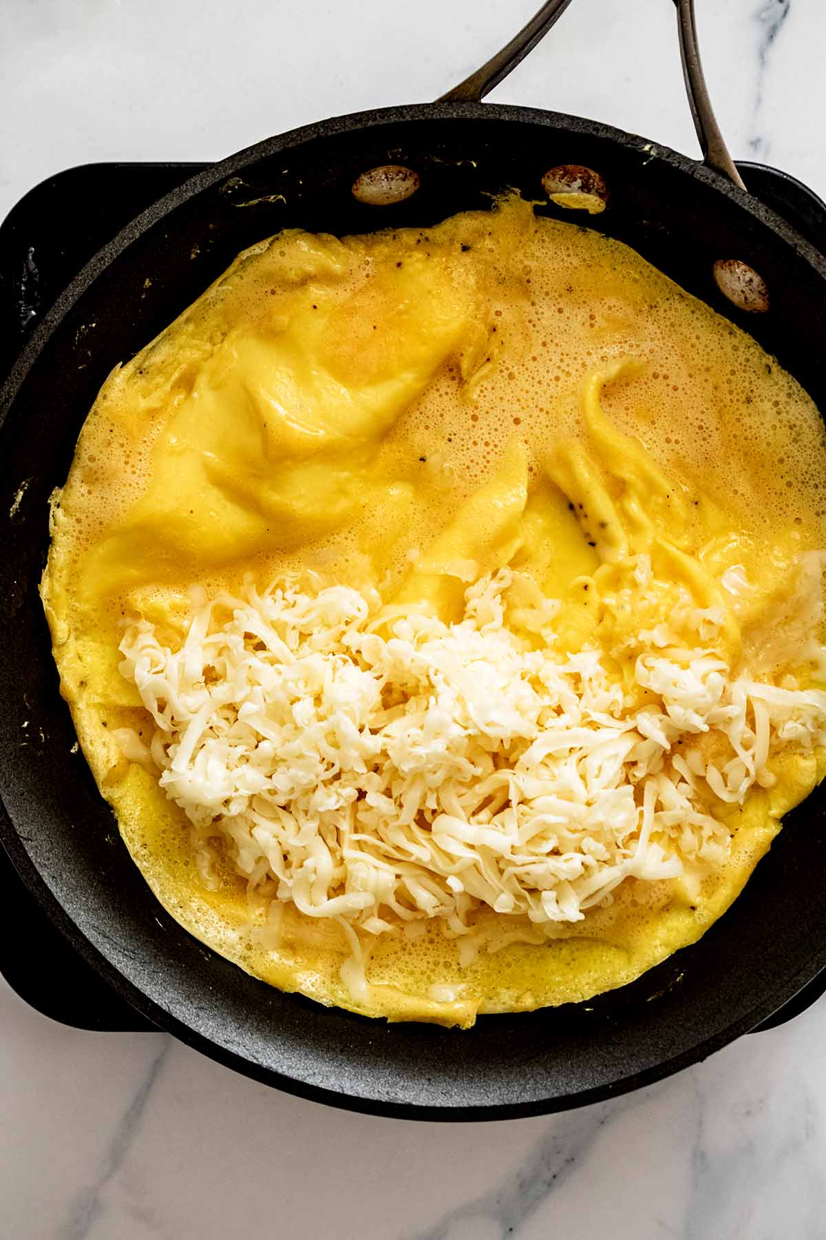 Semi-cooked omelette in a skillet with shredded fontina cheese added to one half of omelette