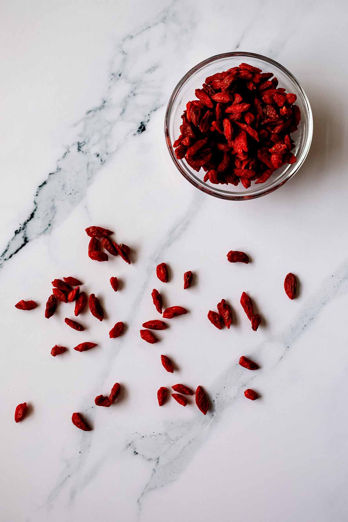 Goji berries on a white marble background with a small glass bowl of goji berries
