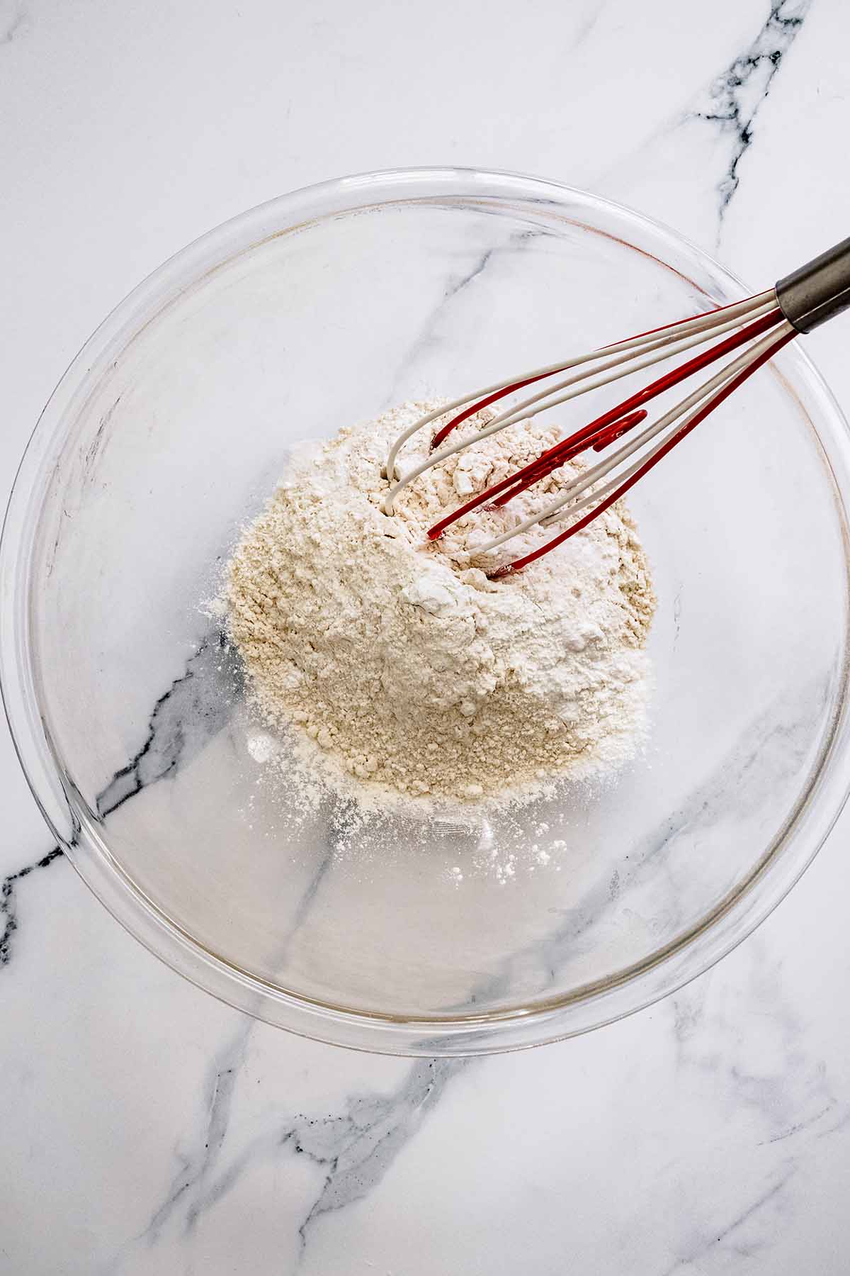 Overhead view of dry ingredients in a glass bowl with a whisk.
