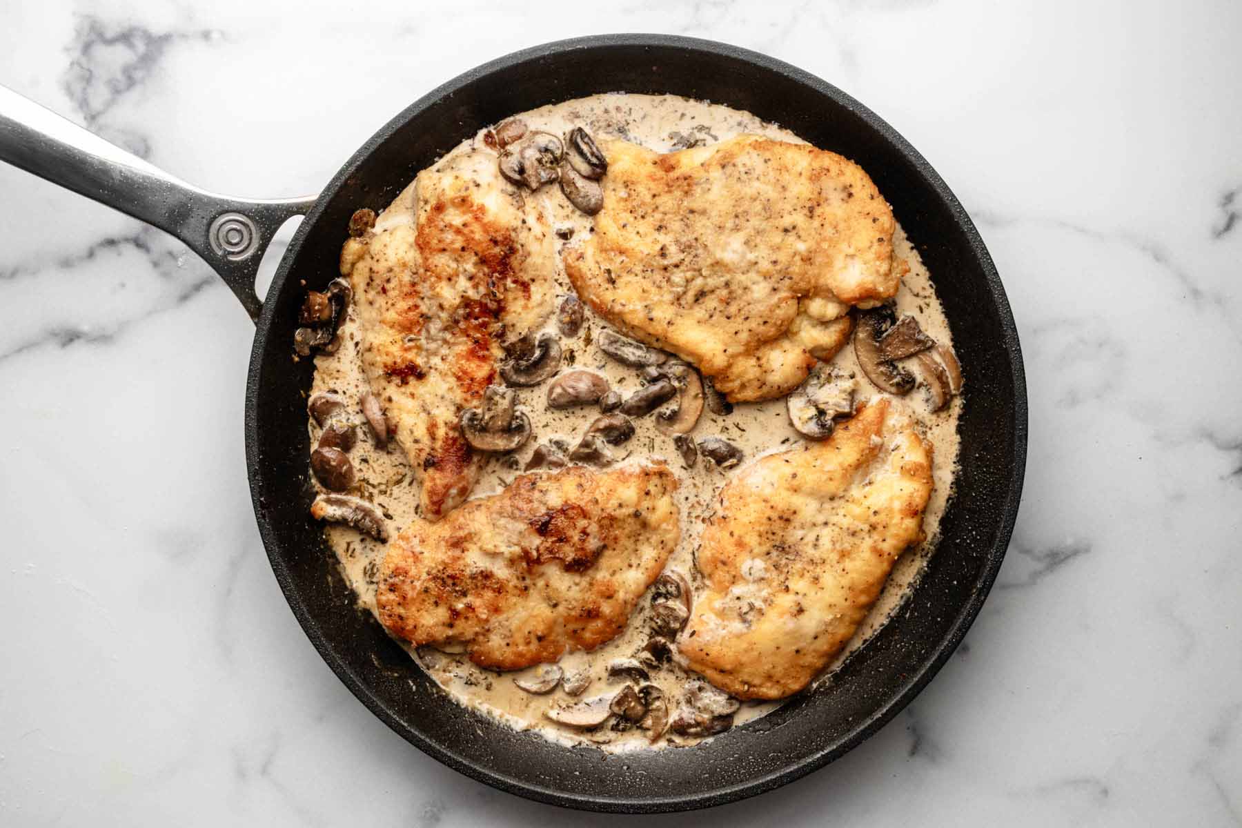 Four chicken cutlets in the skillet with mushroom sauce.