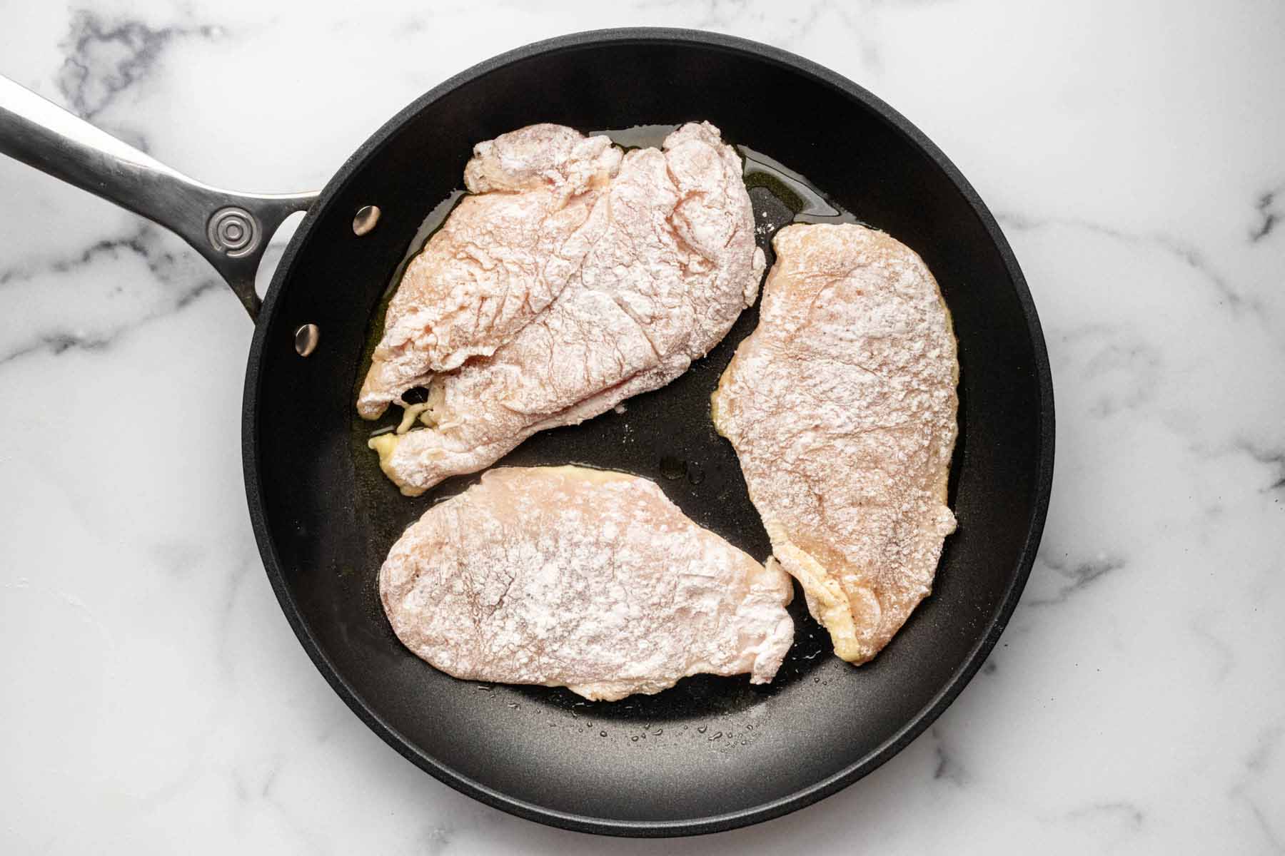 Three chicken cutlets cooking in a skillet