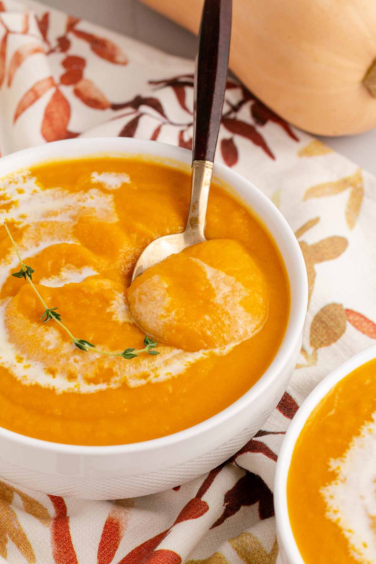 Creamy butternut squash soup in a white bowl with a spoon reaching in to scoop some up.