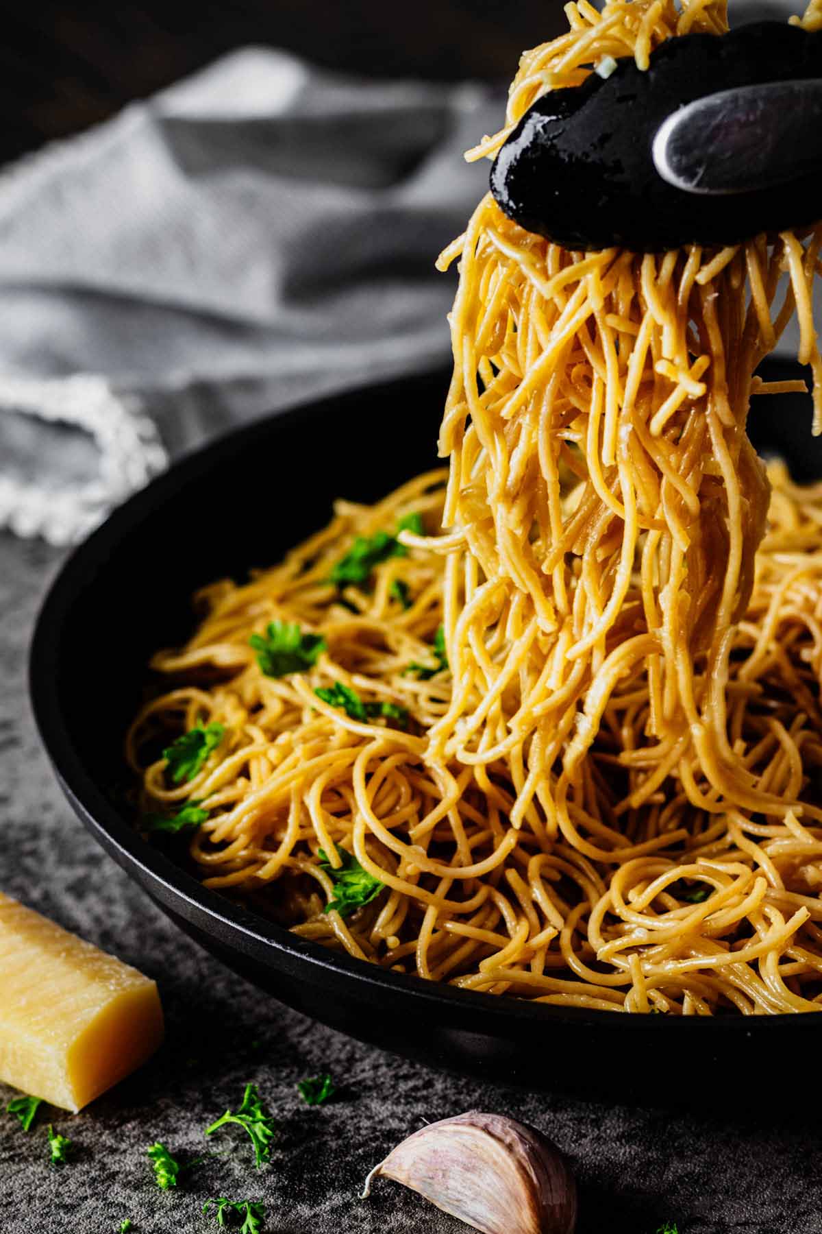 Tongs lifting Parmesan butter noodles from a skillet.