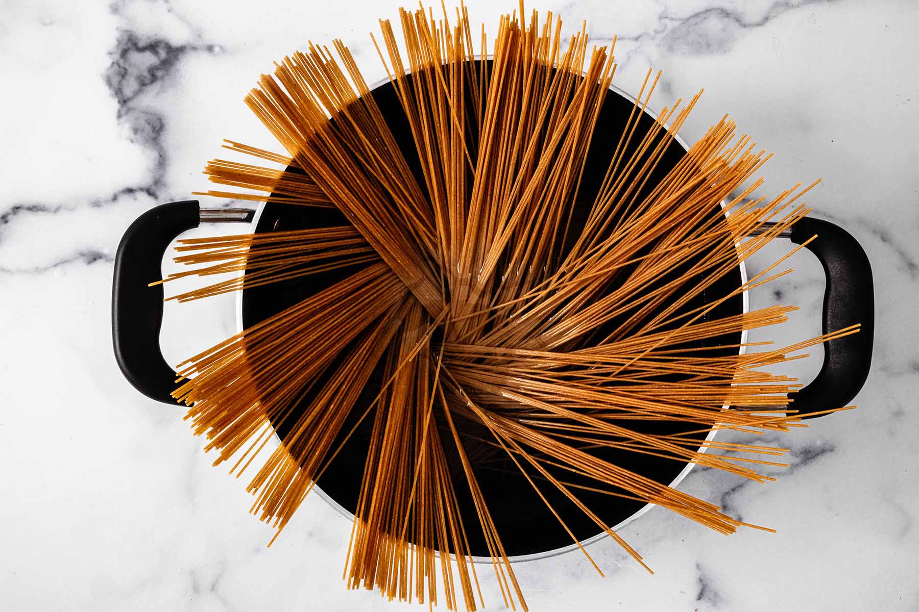 Thin spaghetti sticking out of a large pot of water.