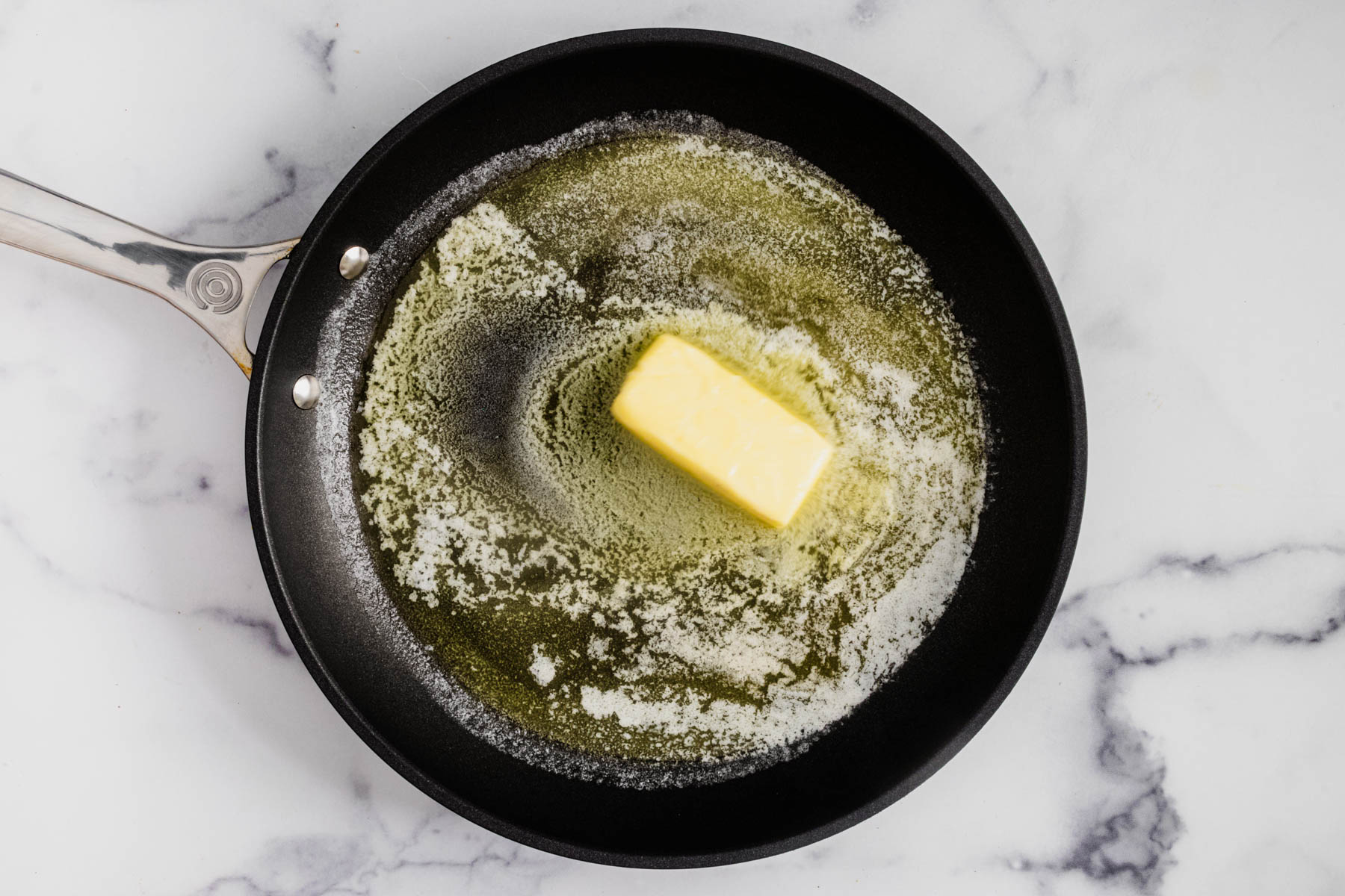 A stick of butter melting in a large skillet.