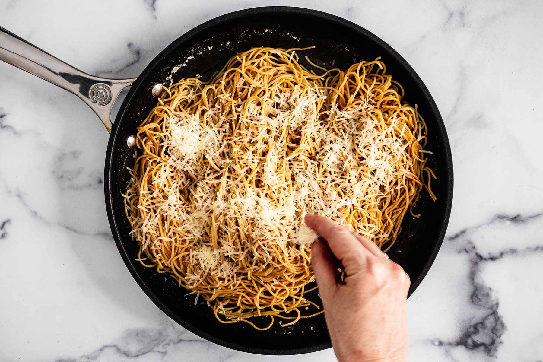 Sprinkling grated Parmesan cheese on top of noodles.