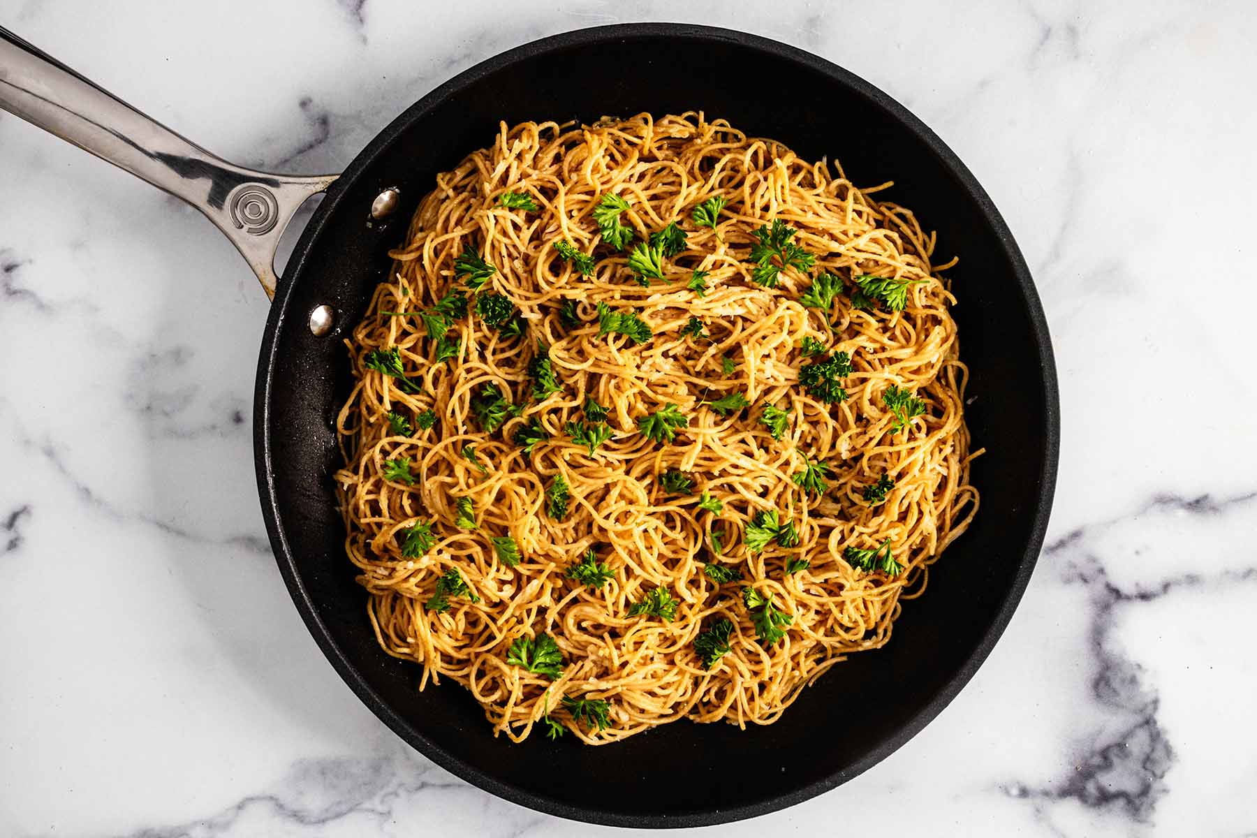 Noodles garnished with curly leaf parsley in a skillet.
