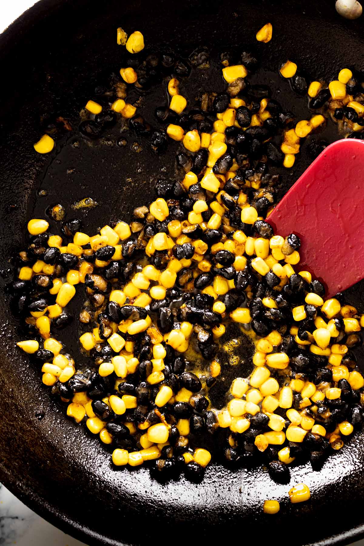Corn and black beans cooking in a skillet with a red spatula.