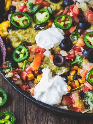 Closeup of scrambled egg breakfast nachos in a cast iron skillet on a dark wood background.