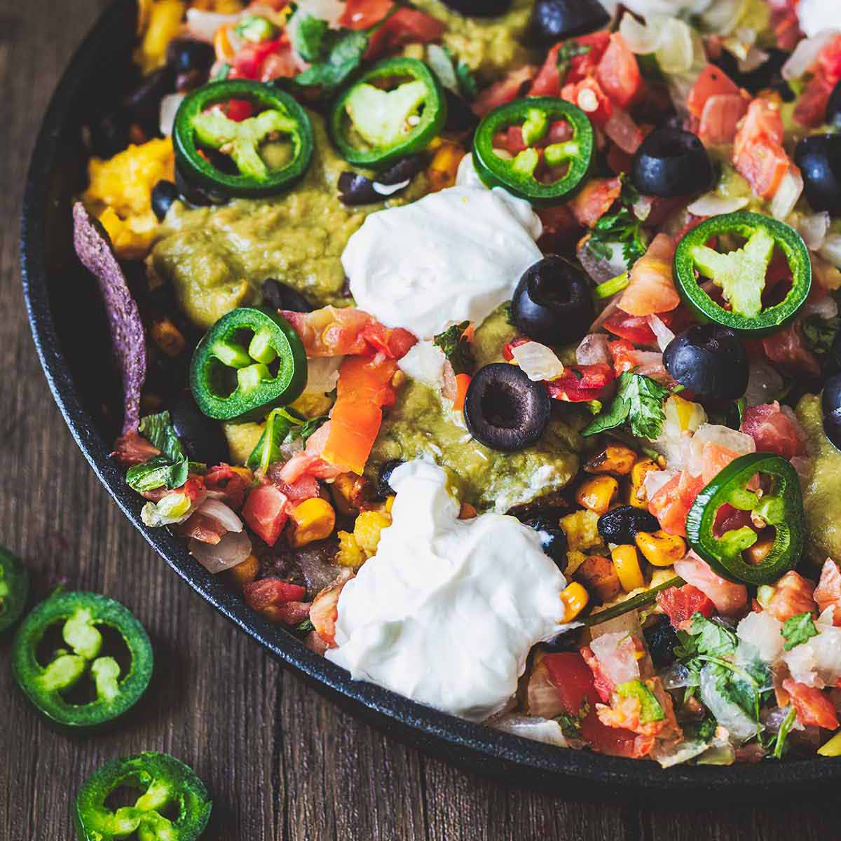 Closeup of scrambled egg breakfast nachos in a cast iron skillet on a dark wood background.