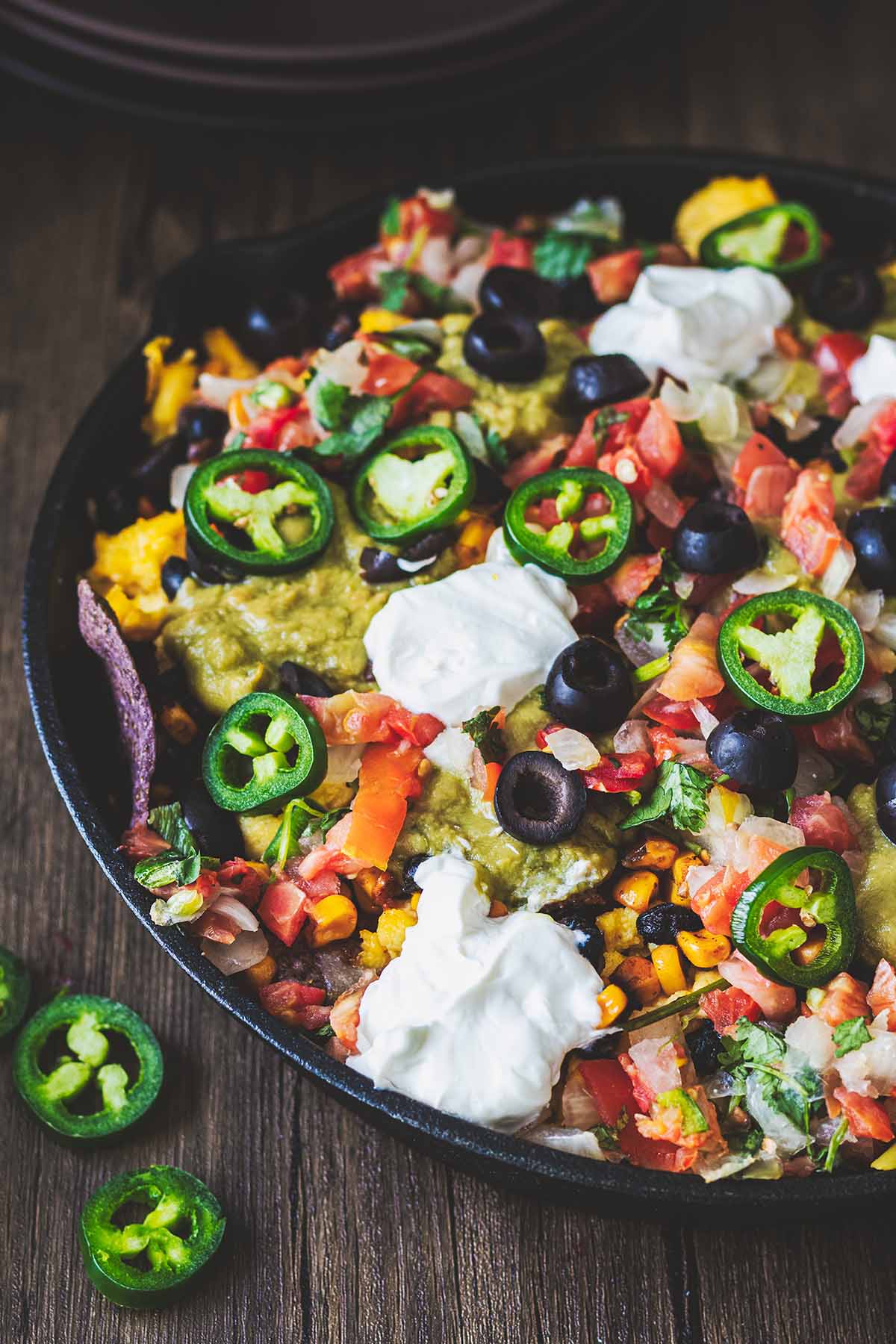 Close up of breakfast nachos in a cast iron skillet on a dark wood background.