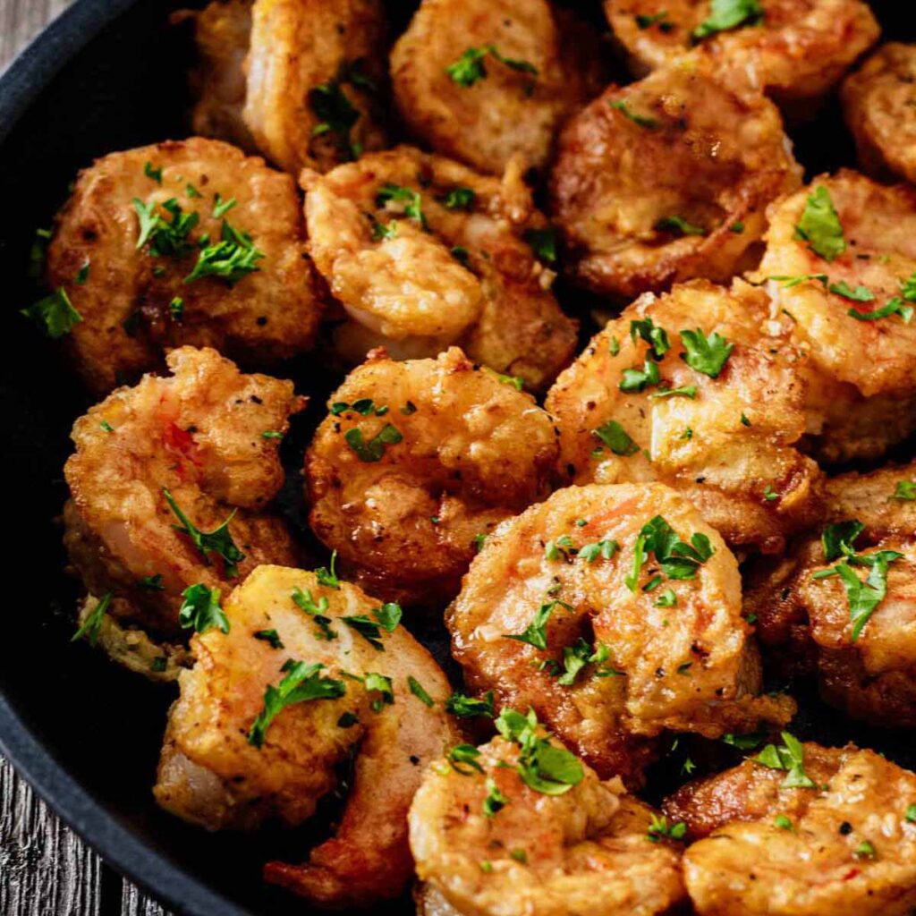 Tight close up of shrimp Francese garnished with chopped parsley in a skillet.