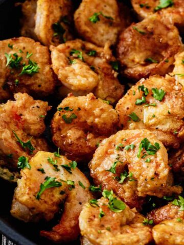 Tight close up of shrimp Francese garnished with chopped parsley in a skillet.