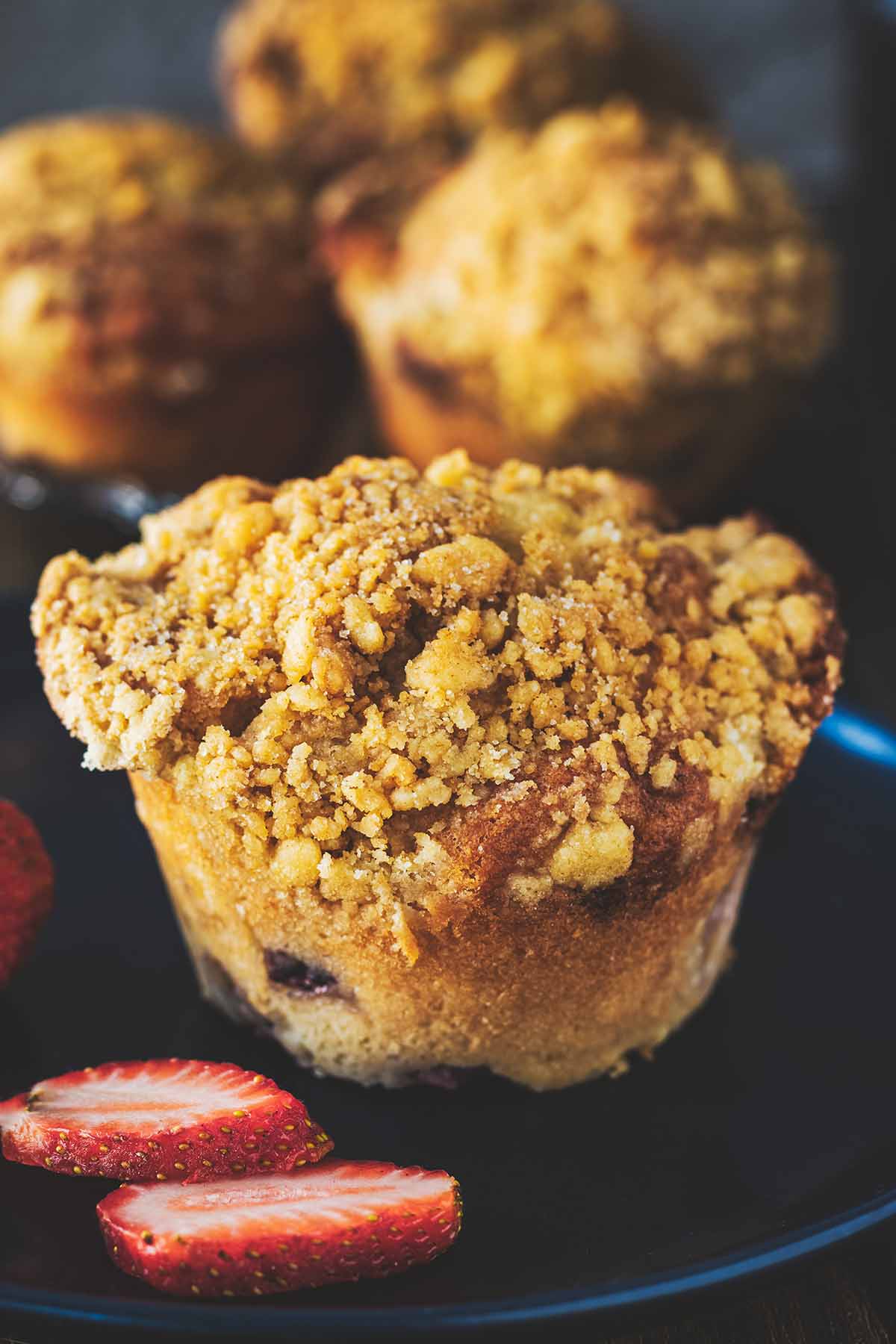 Strawberry muffins with ginger crumb topping on a blue plate with sliced strawberries