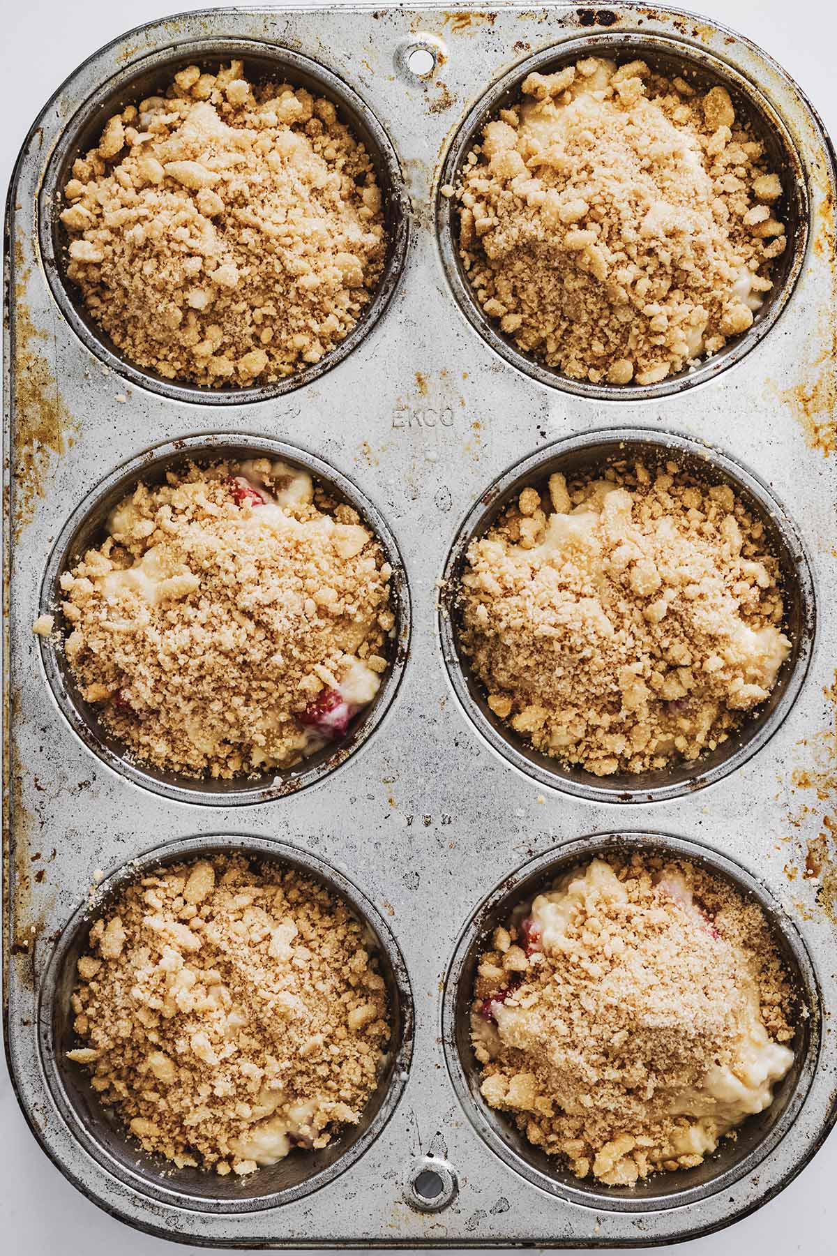 Overhead view of strawberry muffin batter with crumb topping in a muffin tin