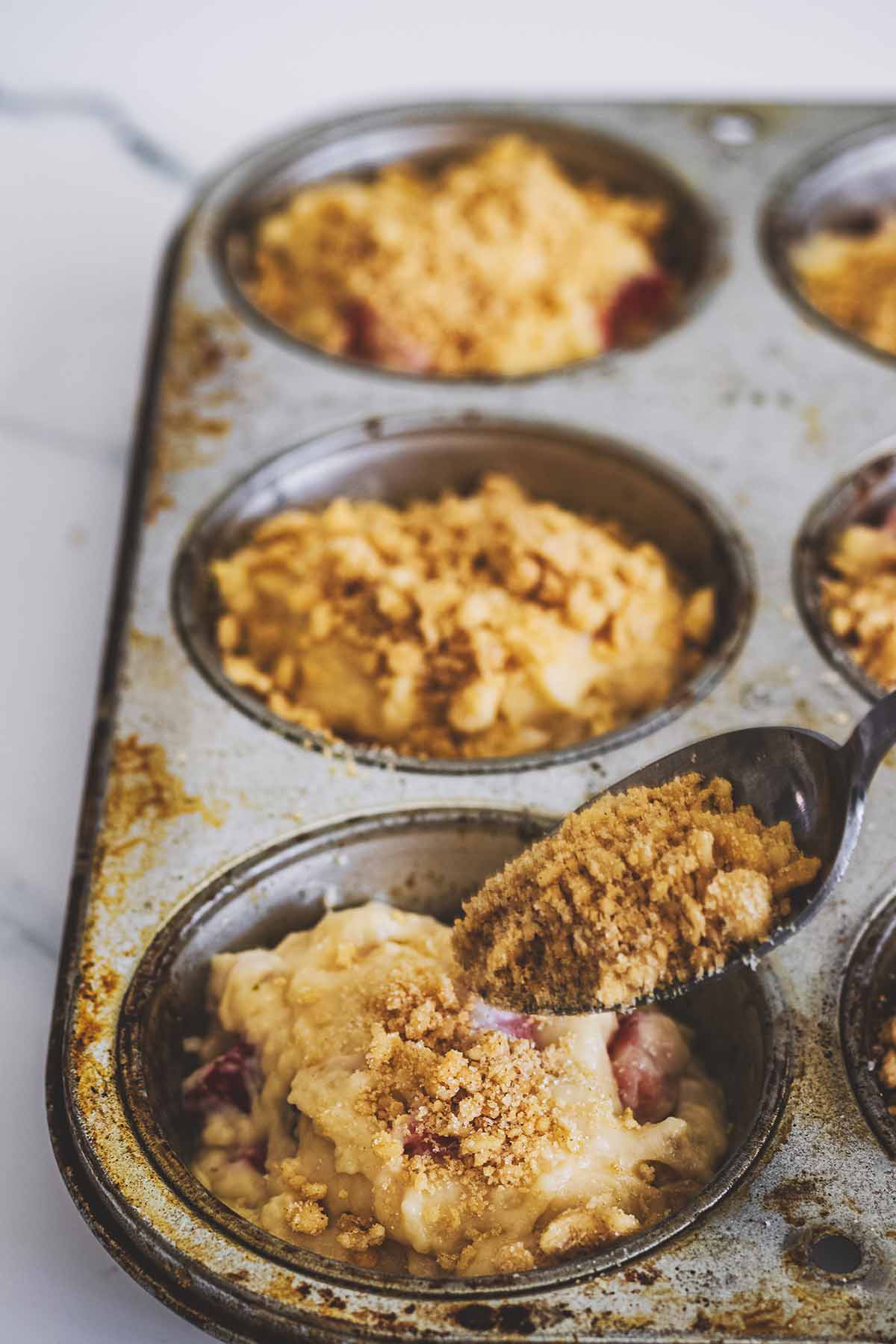 Crumb topping being spooned on muffin batter in a muffin tin