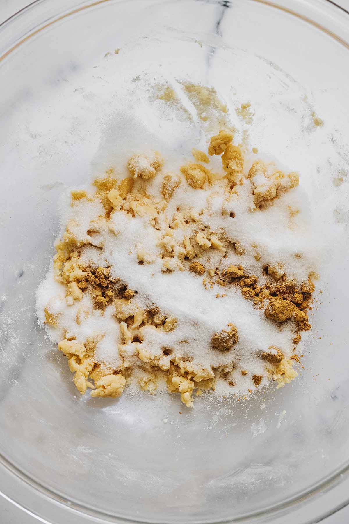 Sugar and ground ginger in a glass bowl with flour and butter crumbles