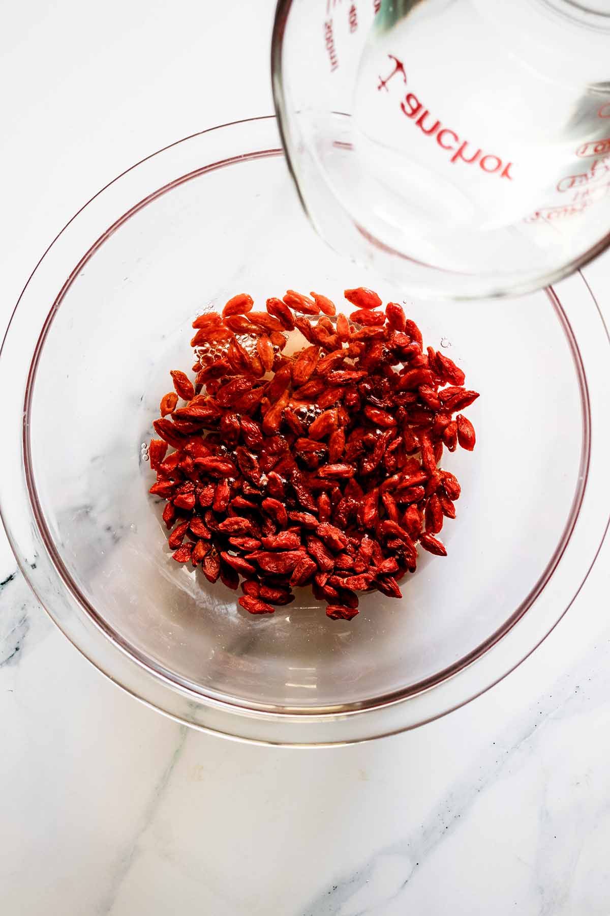 Overhead view of water being added to goji berries in a glass bowl