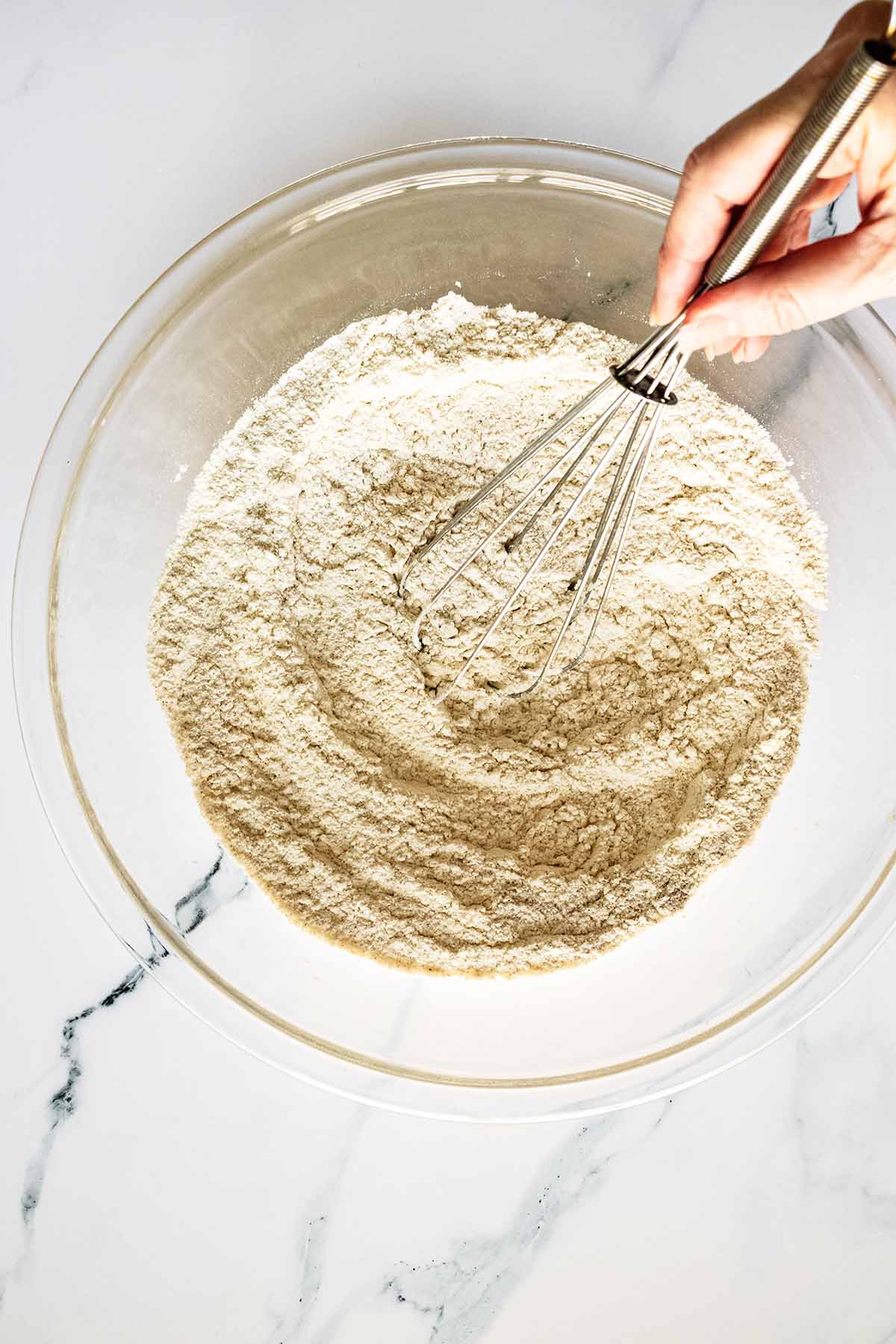 Dry ingredients in a glass bowl being stirred with a wire whisk