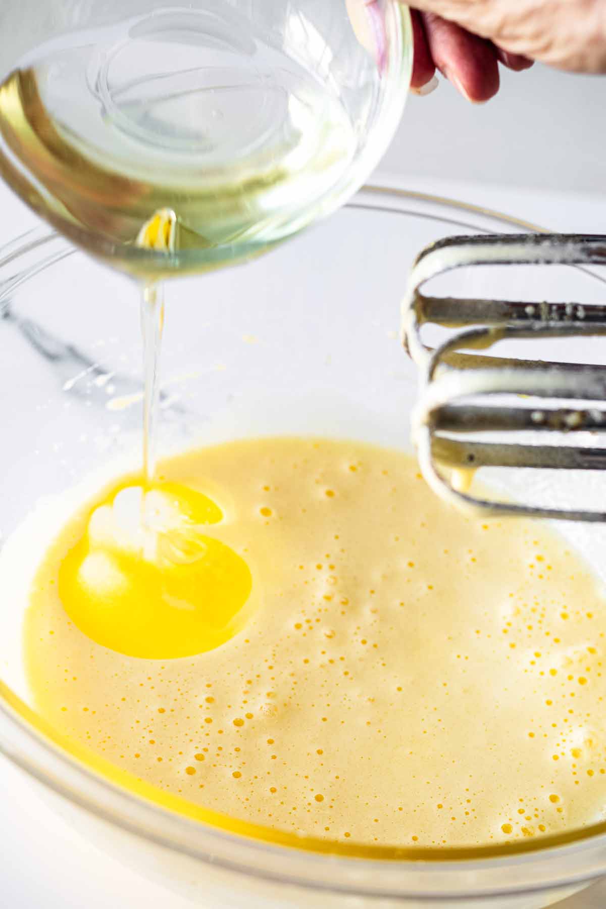 Oil being added to egg mixture in a glass bowl