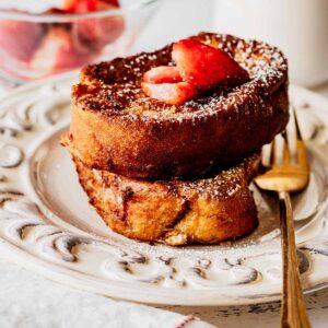 French toast topped with strawberries on a white plate with a gold fork
