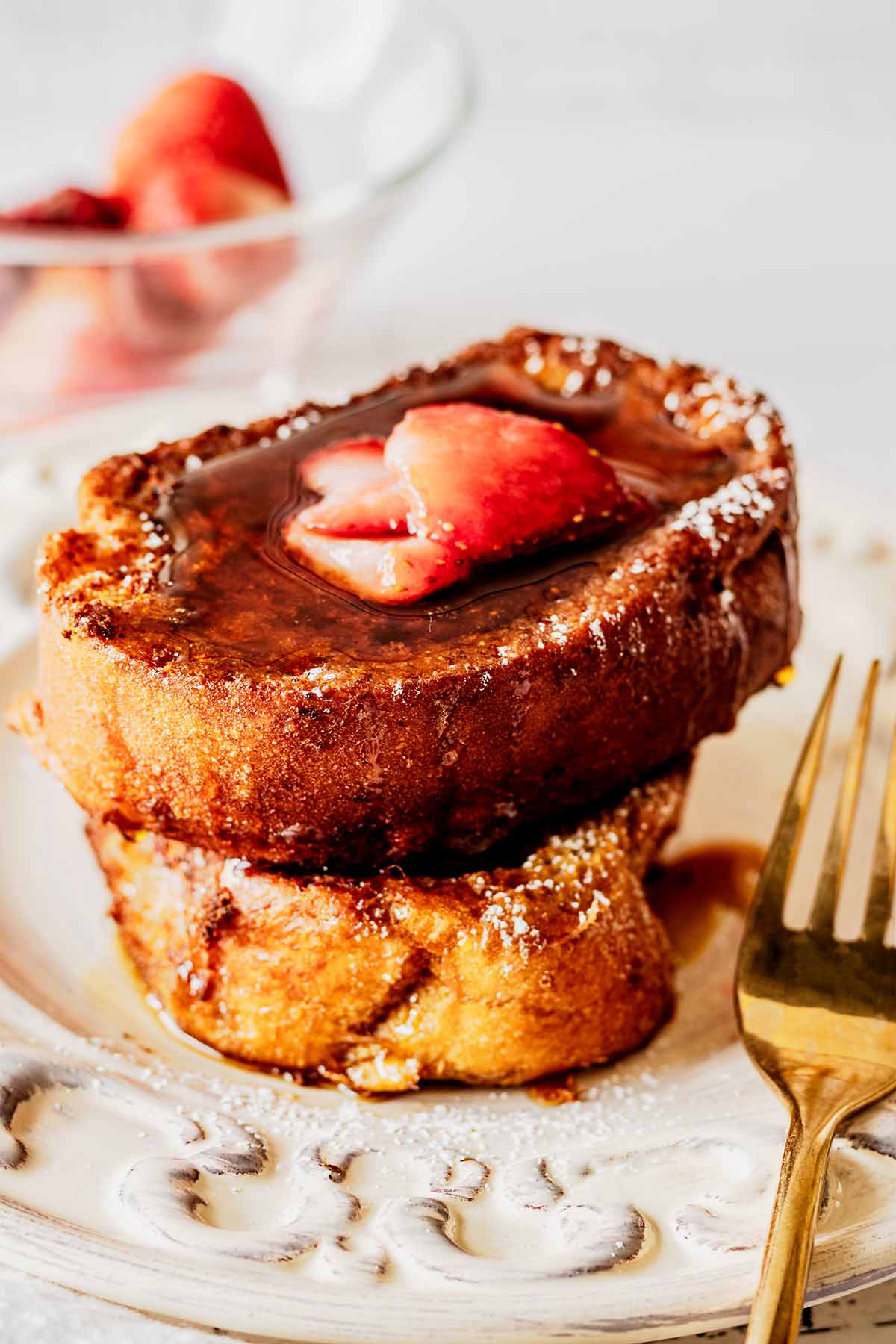 Close up of deep fried French toast on a white plate with a gold fork