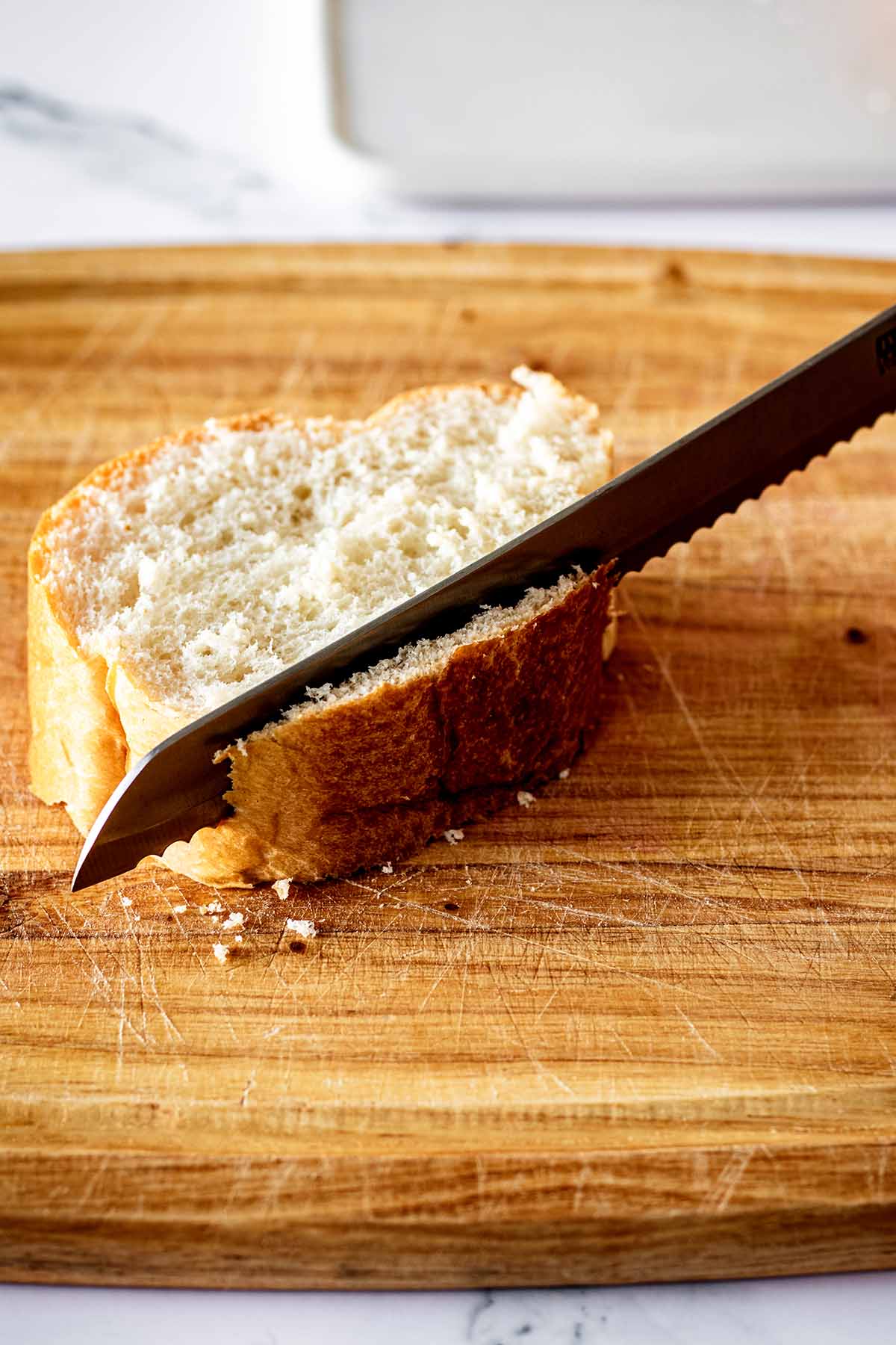 Knife cutting the bottom off of a slice of bread on a cutting board