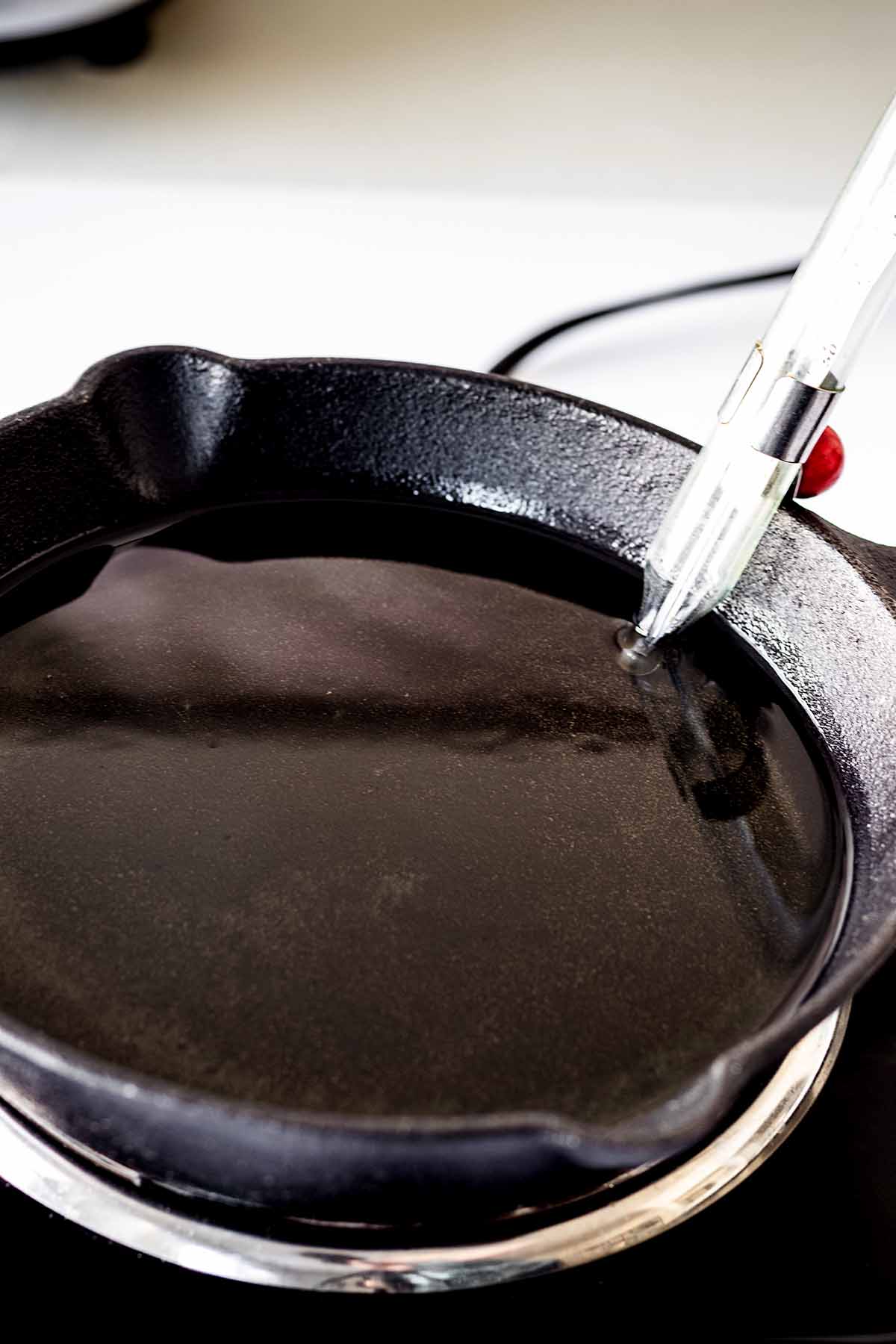 Melted shortening in a cast iron skillet with a thermometer attached to the side