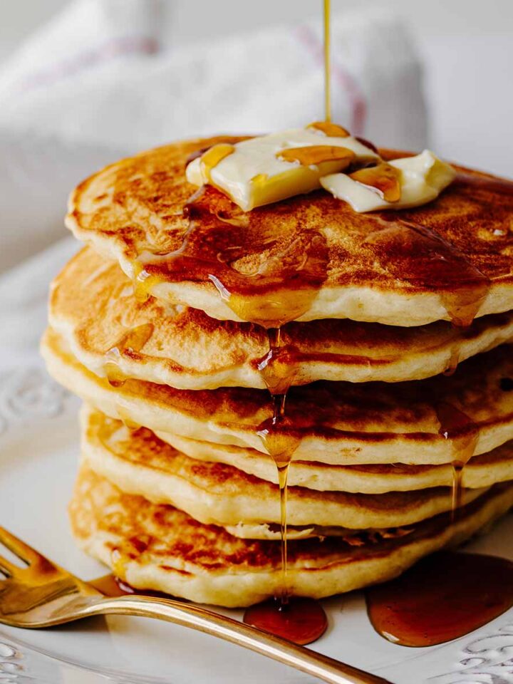 Stack of homemade pancakes with syrup on a white plate