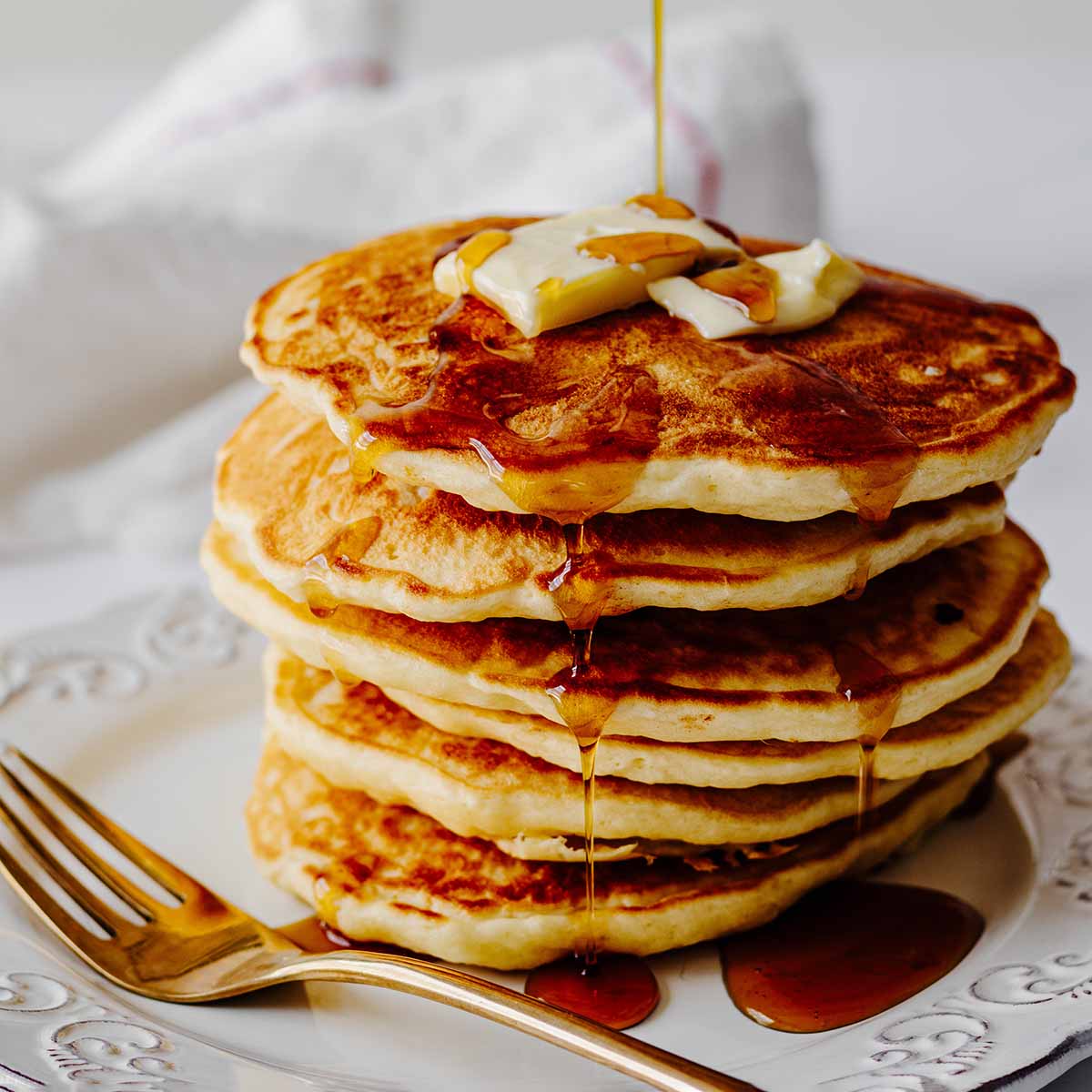 Stack of homemade pancakes with syrup on a white plate